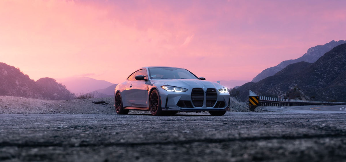 BMW M4 coupe parked on a mountain road at sunset